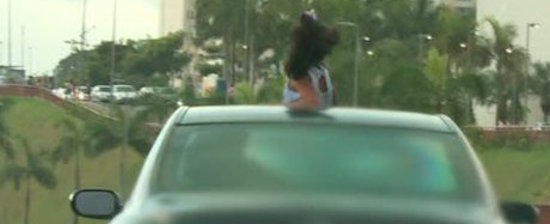 Criança é vista com parte do corpo para fora de carro em movimento