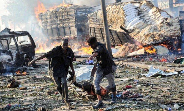 Dois homens arrastam o corpo de uma vítima do bombardeio na capital da Somália (Crédito: MOHAMED ABDIWAHAB / AFP)