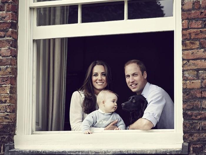 Em foto de 29 de março de 2014, o príncipe William, a princesa Kate, o filho George e o cachorro Lupo posam na janela do Palácio de Kensington, no Reino Unido  (Crédito: AFP)