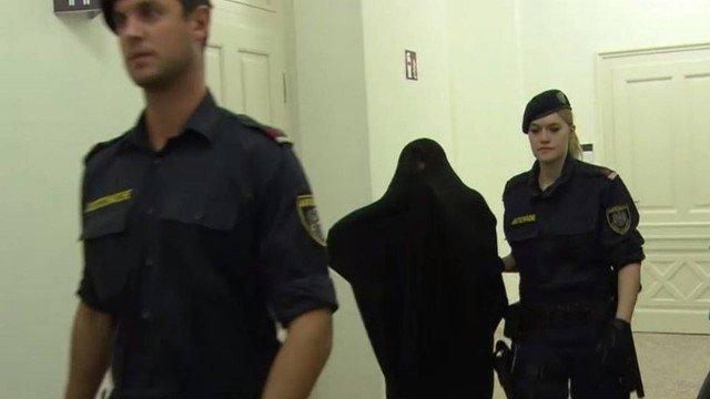 Com o rosto coberto, Silvia M. é conduzida por policiais em tribunal de Slazburgo (Crédito: Reprodução)
