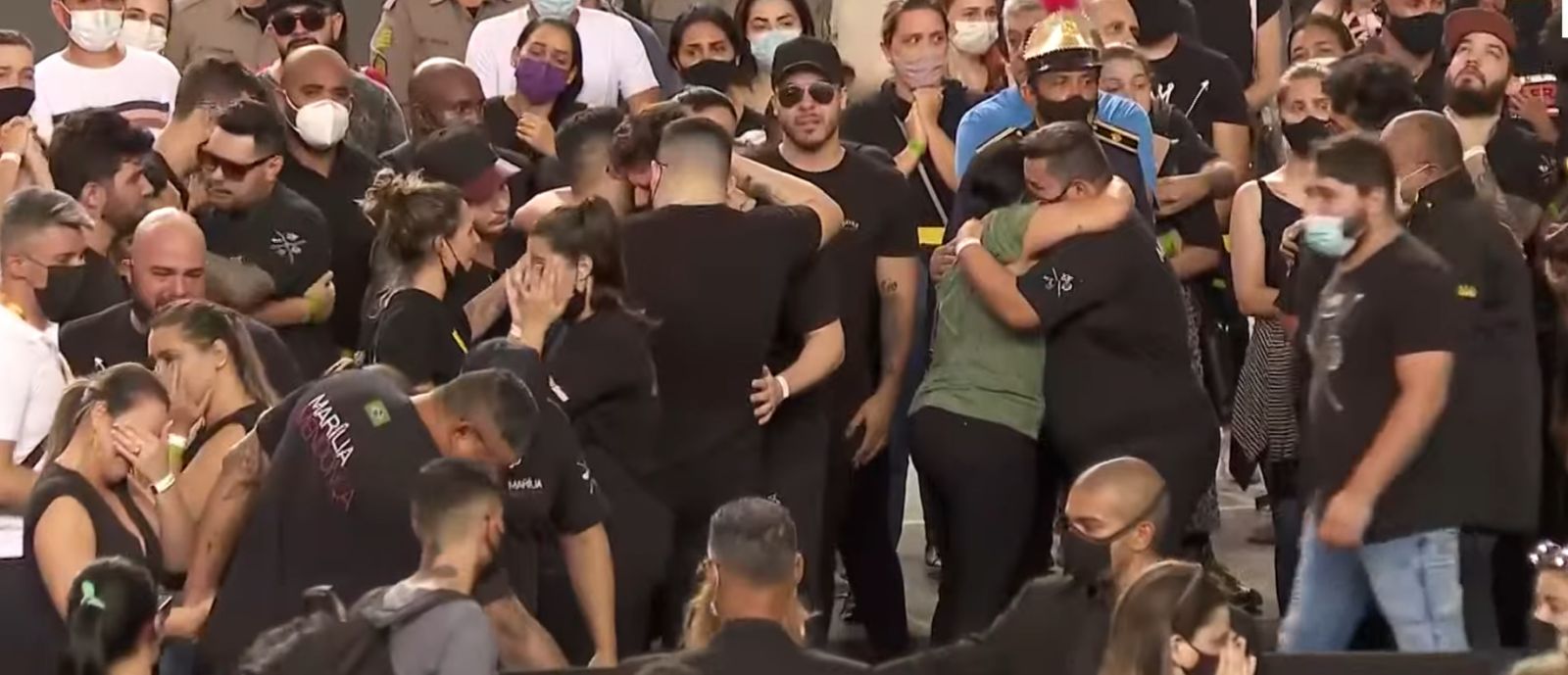 De camisa verde, dona Ruth, mãe de Marília, abrança integrante da banda. Imagem: Reprodução/CNN